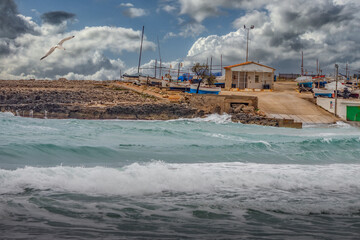 Rustic Coastal Boat Ramp with Boats and Rough Ocean Waves Under Cloudy Sky