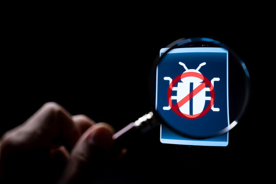 Hand Holding Magnifying Glass Over Bug Icon on Screen, Representing Software Bug Detection and Removal