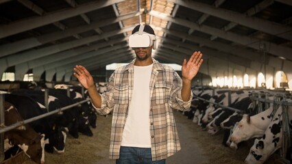 Attractive African American man wearing virtual reality headset. Handsome male standing in cowshed and using digital device. Planning farm building with VR simulator. Concept of innovation technology.