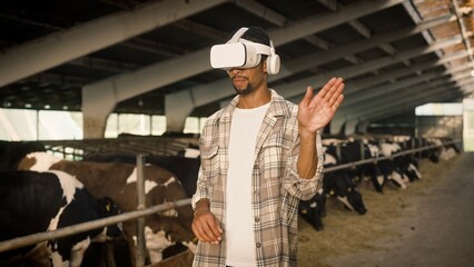 Attractive African American man wearing virtual reality headset. Handsome male standing in cowshed and using digital device. Planning farm building with VR simulator. Concept of innovation technology.