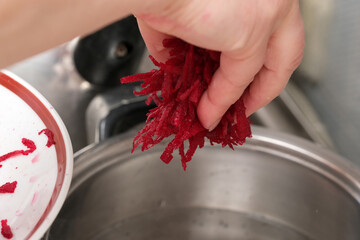 Hand gently adds freshly shredded beets to boiling water for cooking