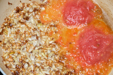 Chopped onions fry in hot oil beside vibrant, fresh tomatoes in a pan