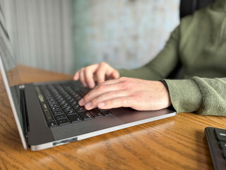 Hands typing on a laptop keyboard on a wooden desk