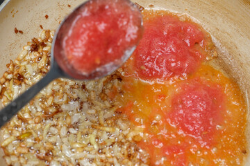 Cooking vibrant tomato sauce with caramelized onions on a rustic stove