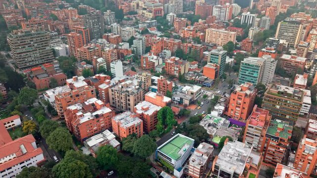 Drone shot over dense Bogot&aacute; with rooftops, buildings, light traffic, roads, and scattered trees.