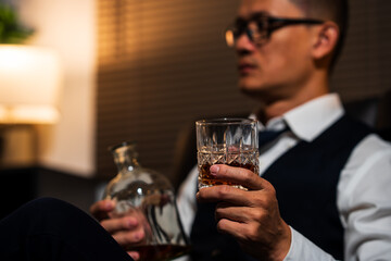 Businessman holding a glass of whiskey, sitting and drinking in a room
