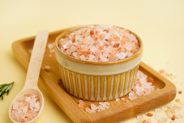 Bowl and spoon with Himalayan pink salt on yellow background