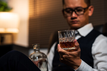 Businessman holding a glass of whiskey, sitting and drinking in a room