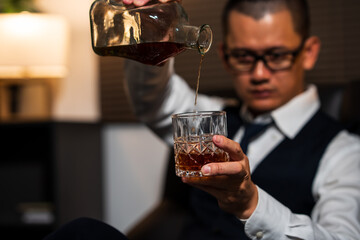 Businessman holding a glass of whiskey, sitting and drinking in a room