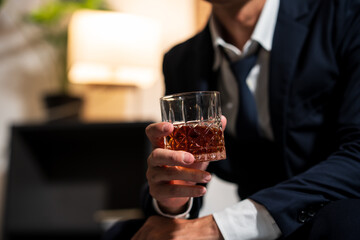 Businessman holding a glass of whiskey, sitting and drinking in a room