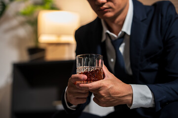 Businessman holding a glass of whiskey, sitting and drinking in a room