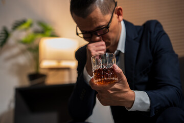 Businessman holding a glass of whiskey, sitting and drinking in a room