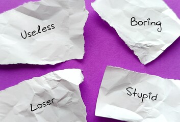 Torn crumples paper with text - LOSER STUPID USELESS BORING - Low self-esteem person tended to use negative labels to describe themselves - self-sabotage by believing unfair negative labels