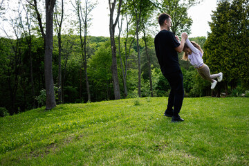 Father spinning his daughter while playing outdoors in a lush green park