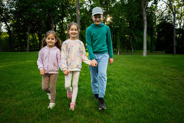 Three smiling children walking together in a park on a sunny day