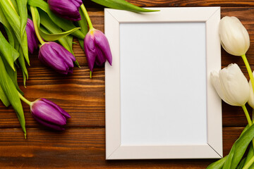 White frame with purple and white tulips on wooden background