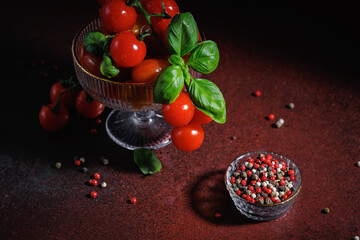 Vibrant red cherry tomatoes and basil leaves styled in a crystal bowl on a rustic surface, ideal...