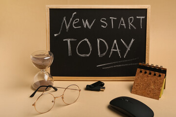 Blackboard with text NEW START TODAY, hourglass and notebook on beige background