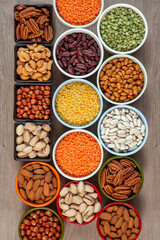 Set of various types of nuts, beans and lentils in multi-colored round ceramic bowls on a wooden table  in multicolour ceramic bowls , top view. The concept of healthy eating and healthy living,