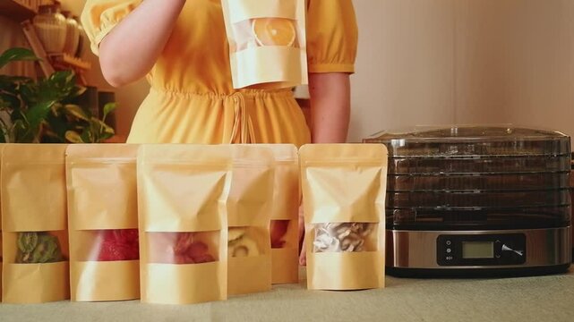 Woman presenting various dehydrated fruits and vegetables packed in doypacks, next to a dehydrator