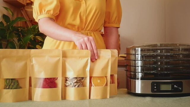 Woman presenting various dehydrated fruits and vegetables in doypacks, next to a dehydrator