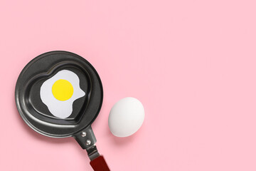 Composition with egg, frying pan in shape of heart and fried egg on pink background
