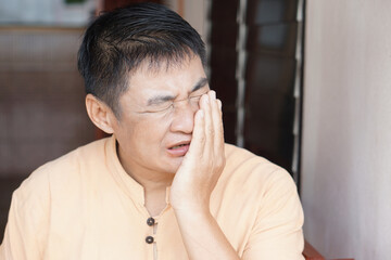 A middle-aged Asian man suffering from a severe toothache. His painful facial expression and hand...