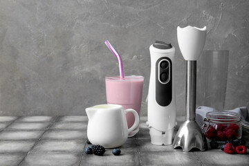 Modern blender with glass of smoothie, jug and berries on grey tile table
