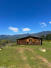 A wooden cabin with Snow-Capped Peaks in the mountains on a sunny day. Rustic Cabin. Scenic view of rolling hills, mountains, and a cloudy sky under sunlight.