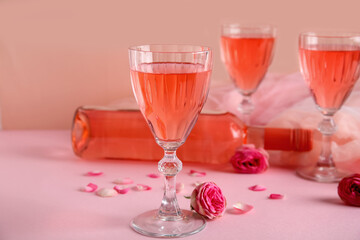 Glasses and bottle of tasty pink wine with beautiful roses on color background