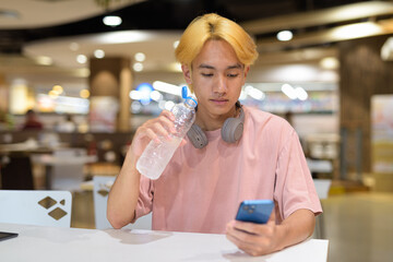 Young student teenager man with headphones drinking water and using mobile phone