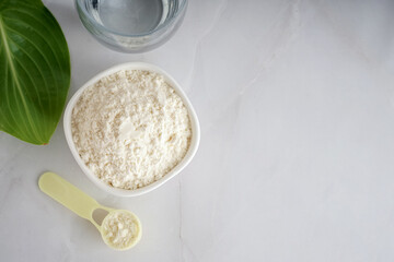 Scoop and bowl with collagen powder and glass of water on white background