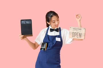 Young Asian waitress with blackboard and signboard with text WELCOME WE'RE OPEN on pink background