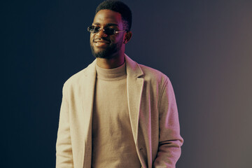Stylish young African man in a trendy coat and sunglasses, radiating confidence against a gradient backdrop, perfect for fashion and lifestyle themes