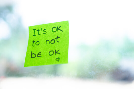 Green sticky note reminding it's okay to not be okay with blurred background