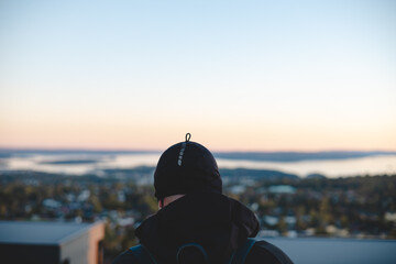 Overlooking Oslo from above, a traveler watches the sunset paint the horizon in peach and blue, embracing a serene Scandinavian evening from the heights