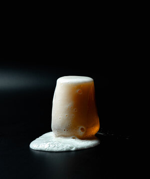 Foam pouring from a glass of beer on a dark background