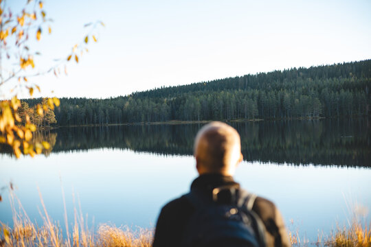 50 years old backpacker watch lake in Oslo Marka, where calm reflections and golden light embrace the silence of Scandinavian wilderness during sunset
