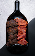 Jerky meat snacks on a plate with a bottle of wine isolated close-up on a contrasting background