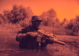 Soldier in camouflage gear and hat, holding a rifle, wading through a swamp with trees in the background under an orange-tinted sky.