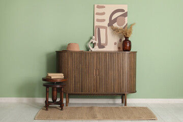 Chest of drawers with pampas grass, picture and books on stool near green wall in room