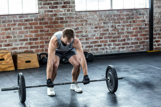 Barbell resting on rubber gym floor, near plyo boxes and kettlebell under industrial windows