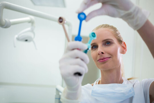 Female dentist examining 3 color-coded dispensing tips in clinic with dental lamp arm, copy space
