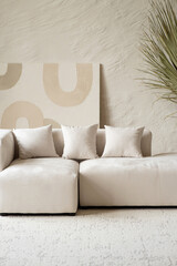 A spacious living area showcases a contemporary sectional sofa adorned with cushions, complemented by a large dried palm plant in a bright and airy setting.
