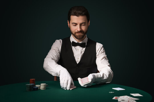 Handsome male banker with poker chips putting playing cards on table in casino