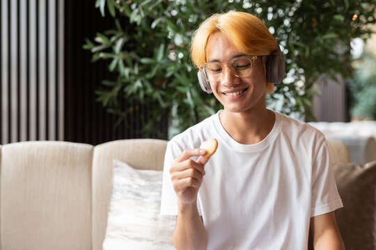 Asian teenager man with blonde hair inside cafe restaurant eating cookie