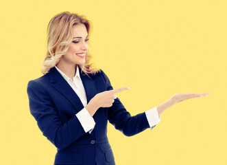 Portrait image - happy smile businesswoman show point hold some product, advertise. Business woman executive employee bank manager, teacher isolate orange yellow background with ad free space