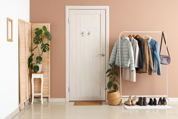 Interior of stylish hall with clothes rack, houseplants and key holder on door