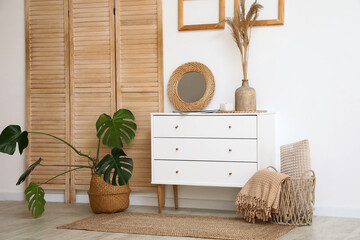 Interior of living room with chest of drawers and folding screen near white wall