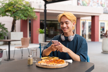 Thai gay teen male enjoying pepperoni pizza in outdoor restaurant